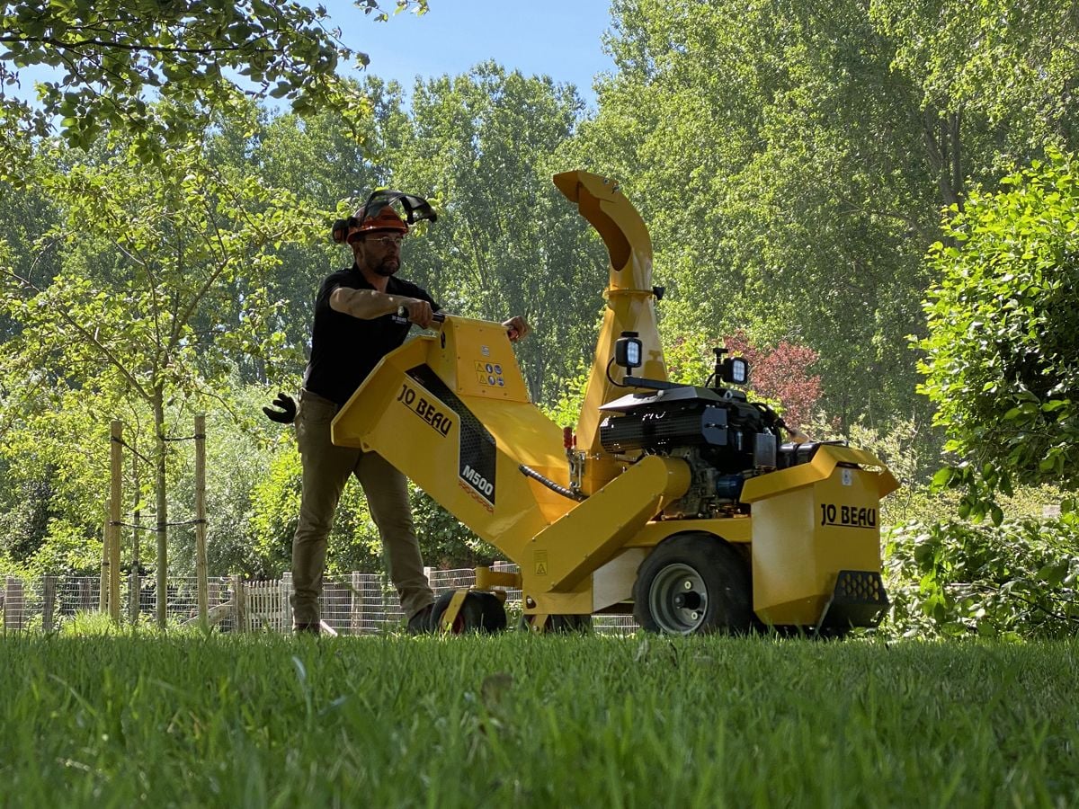 Man gebruikt een professionele hakselaar op benzine voor takken tot 12 cm in een groene tuin.